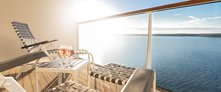 Der Balkon einer SPA-Balkonkabine von Mein Schiff öffnet den Blick in die Weite. Im Gegenlicht taucht die Sommersonne den Außenbereich in warmes Licht.